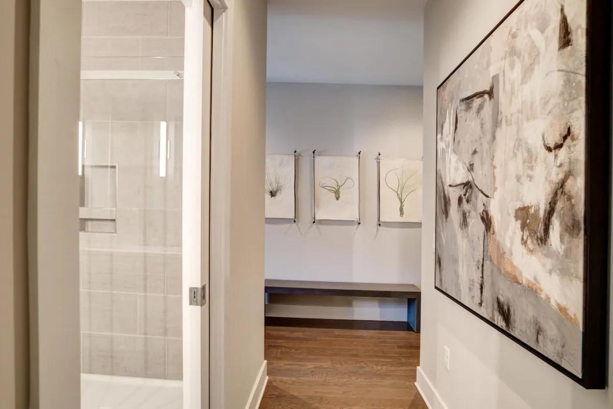 A tranquil building common area with decorative wall hangings, modern artwork, and a wooden bench, designed for relaxation or short waits. The contemporary decor suggests a well-cared-for property and reflects a calm, professional environment.