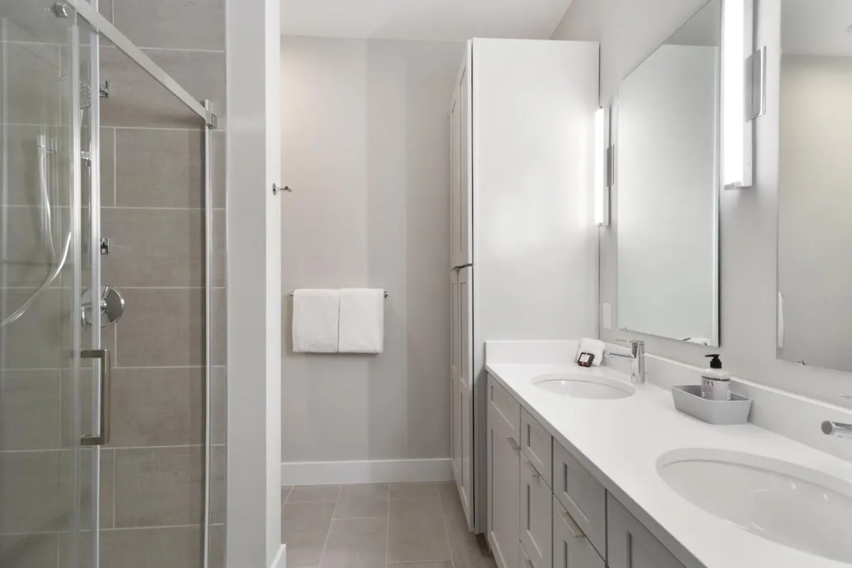 A sleek en-suite bathroom with a double sink vanity, expansive mirrors, and a glass shower enclosure. The space is bright, modern, and designed for self-care rituals, reflecting comfort and convenience.