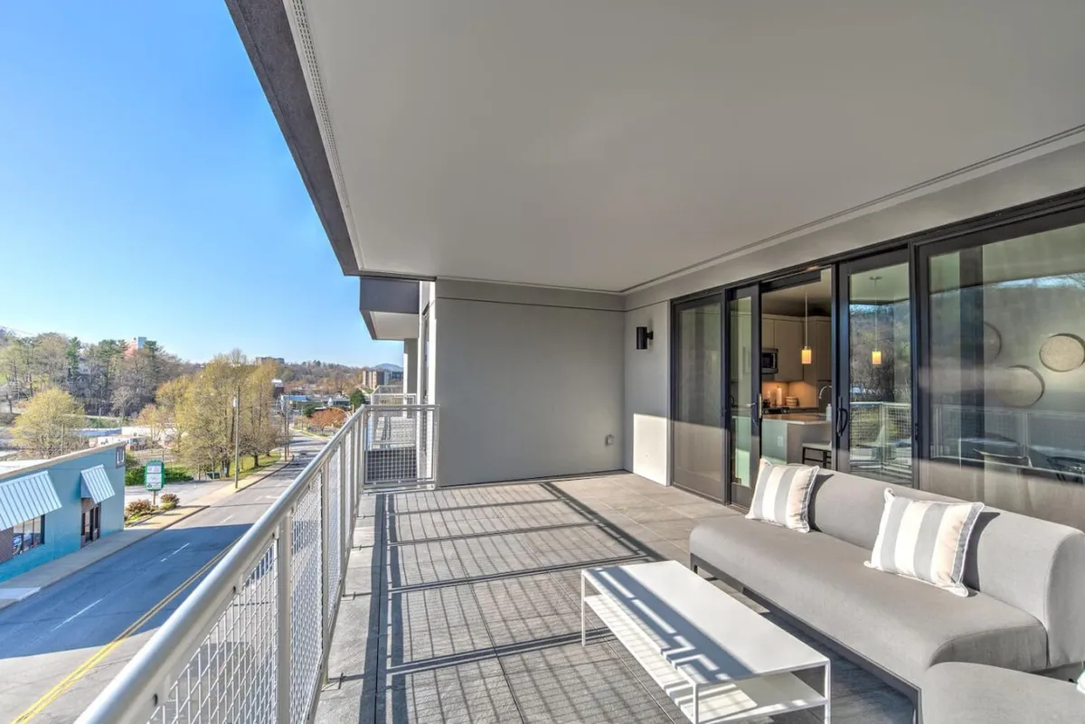 This exterior image shows a balcony outfitted with comfortable furniture and a modern railing, overlooking a lively street scene. The vantage point allows for people-watching and soaking up the city’s vibrant atmosphere, with ample space for outdoor dining or relaxing with a coffee as the city wakes up.