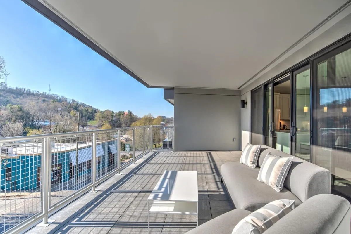 This exterior shot captures a modern balcony seating area with inviting chairs and a sleek railing, set against a backdrop of the surrounding landscape. The scene suggests relaxation, sunrise views, and evenings spent stargazing, underscoring the condo’s elevated position within the city.