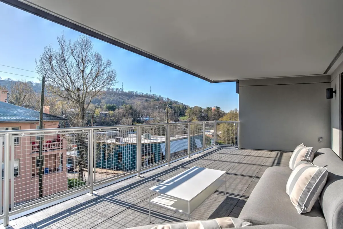 A serene balcony space featuring comfortable seating, a minimalist coffee table, and sweeping views of distant hills. The ambiance is peaceful, with morning light streaming in, showcasing the blend of urban buzz and natural beauty available from the condo.