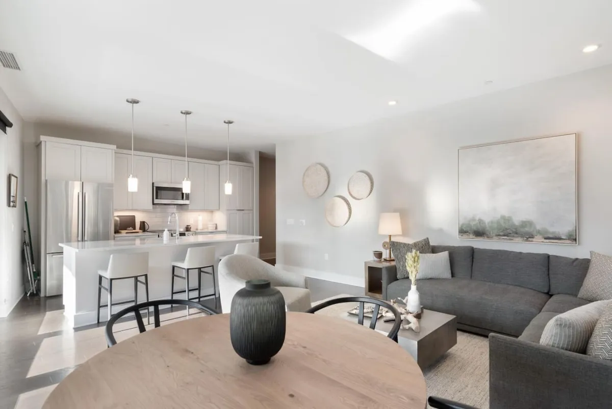A cozy dining area seamlessly connected to the kitchen, featuring a dining table with a decorative vase, a nearby sofa for relaxing, and a kitchen island in view. The ambiance is welcoming, making it ideal for intimate meals or lingering over a glass of wine.